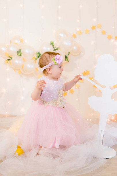 Cute little girl in a pink princess dress with a flower on her hair plays with wooden ballerinas among the golden stars on the background of a large white wooden moon and balloons. Children's decor.  - Foto, Imagen