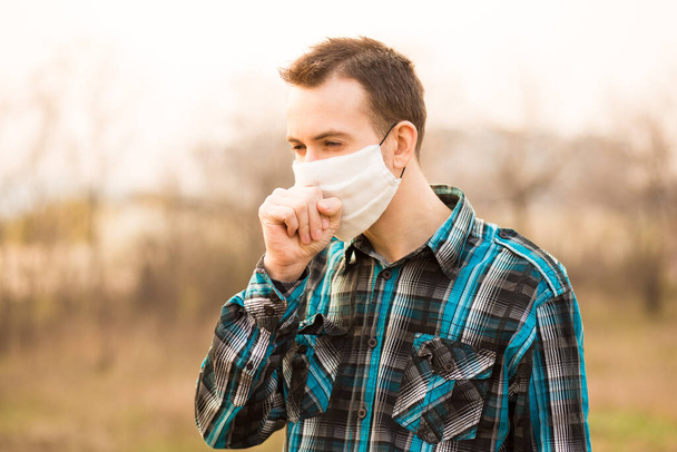 Grippe, concept froid. Portrait de jeune homme se sentant malade, toussant, portant un masque facial en plein air
 - Photo, image