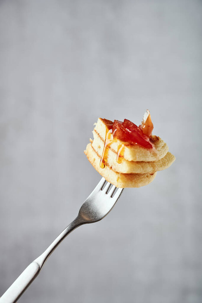 Piece of American-style pancakes stack with apple jam and runny honey on a fork against grey background, with honey drops running down - Foto, afbeelding