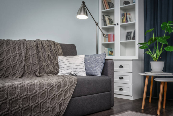 Grey couch with cushions, knitted plaid  and  floor lamp in the room with blue walls - Foto, afbeelding