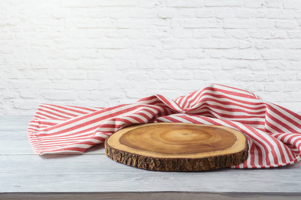 Empty wooden table with tablecloth and wooden board over white brick wall background. Kitchen mock up for design - Fotografie, Obrázek