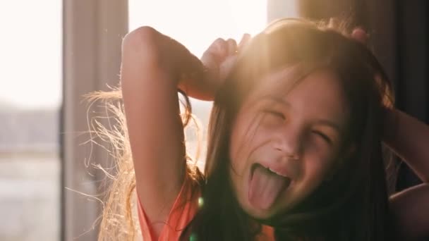 Portret brunetki na tle zachodzącego słońca. Piękne dziecko patrzące w kamerę, śmiejące się i robiące miny - Materiał filmowy, wideo