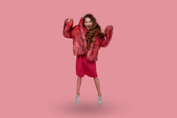 Beautiful young girl dancing in a long pink coat on a pink background. - Photo, image