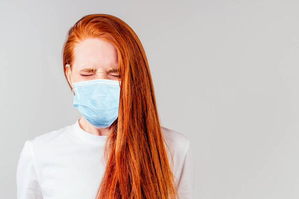 fingers crossed wishing the best in studio gray background redhair ginger woman feeling unhappy and wearing medical mask - Foto, imagen
