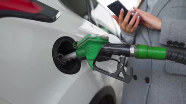 Woman using smartphone while her car is refueling - Footage, Video