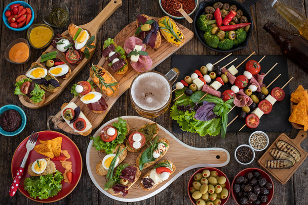 Many tapas on the rustic wooden table with black background. Top view mediterian food concept. - Photo, Image