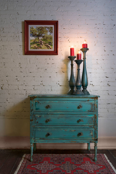 Gabinete vintage verde, candelabros y pintura colgada en la pared de ladrillos
 - Foto, Imagen