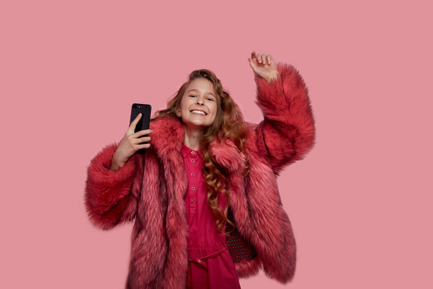 girl dancing with a phone in her hands in clothes in a fur coat with fur - Фото, изображение