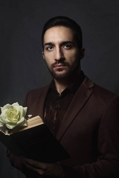 Романтично. Портрет парня. В руках книги и белого цветка. Парень в коричневом костюме. Фото в стиле старой живописи
 - Фото, изображение