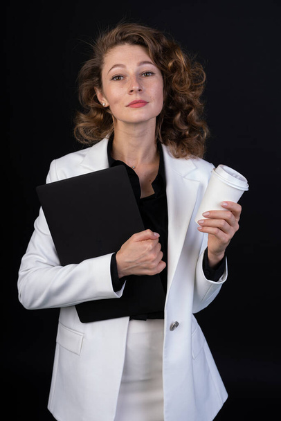 A young woman in a business suit with a document case in one hand and tea in another, curly hair, a distant look - Photo, Image