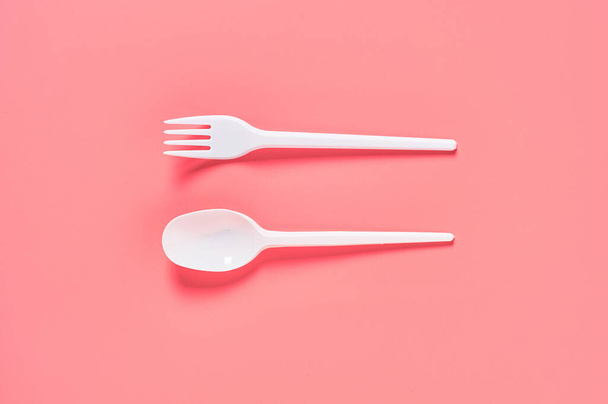 White disposable spoon and fork on pink background. Concept of save environment, ecology, recreation on picnic, party and other events. Top view - Foto, immagini