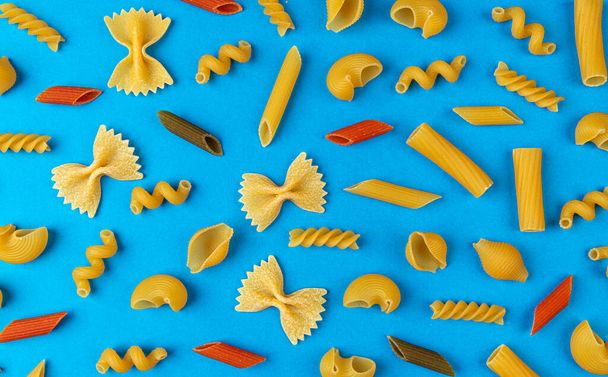 Różne rodzaje makaronów na niebieskim tle, płaska kompozycja świeckich włoskich składników żywności koncepcji, widok z góry suszone mieszane makarony wzór na stole kolor - Zdjęcie, obraz