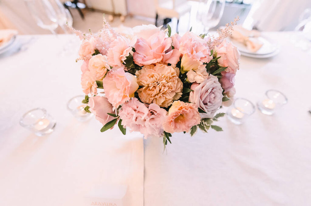 Peach pink floral arrangement. Banquet, restaurant. Table setting. White plates with a gold rim, golden cutlery, glasses.  - Фото, изображение