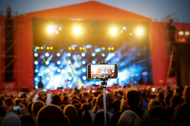 自撮りモノポッドスティック上のスマートフォン。コンサートショーの背景 - 写真・画像