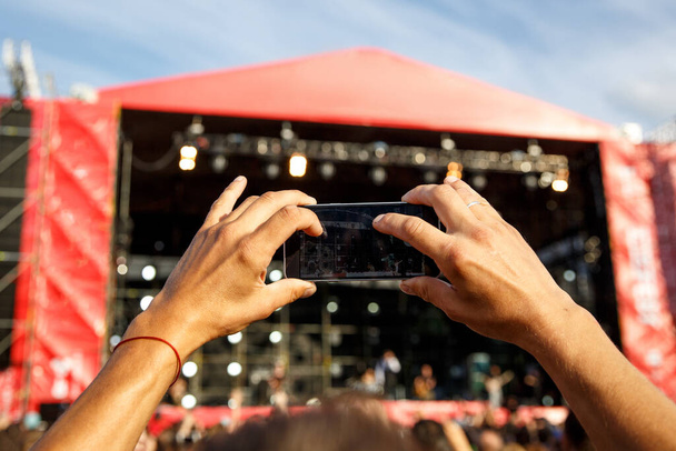 Hombre sosteniendo teléfonos inteligentes en las manos y fotografiando. Tomar fotos en el escenario delantero en el festival de conciertos de música al aire libre de verano. Etapa roja
 - Foto, Imagen
