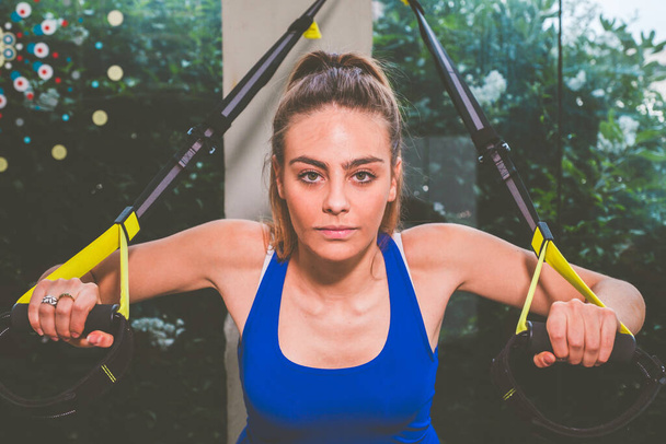 Krásná dívka trénuje své paže s řemínky Trx Fitness v tělocvičně - Žena dělá push-ups vlaky horní části těla hrudníku ramena hrudní triceps - Fotografie, Obrázek