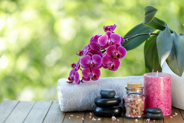 Spa composition on wooden table with zen stones, orchid, bottle of salt, candle and towel. Blurred background with copy space - Photo, Image