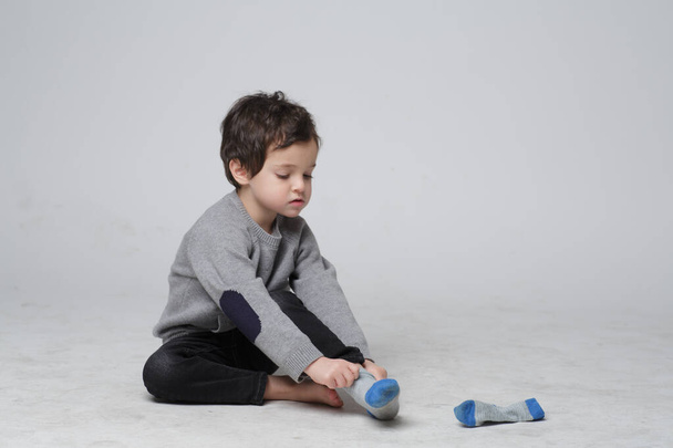 Portrait von niedlichen kleinen Kind sitzen lernen, wie man die Socken von ihm selbst anzieht, Glückliches Kind zieht Socken an seinem Fuß. Kompetenzentwicklung bei Kleinkindern. - Foto, Bild
