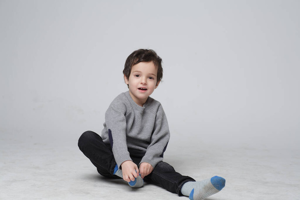かわいい小さな子供の肖像画は、彼自身で靴下を置く方法を学ぶ座って、幸せな子供は彼の足に靴下を引っ張る。幼児概念における技能開発. - 写真・画像