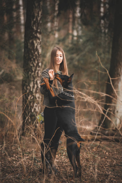 Young girl playing with doberman dog in the forest - Foto, Imagen
