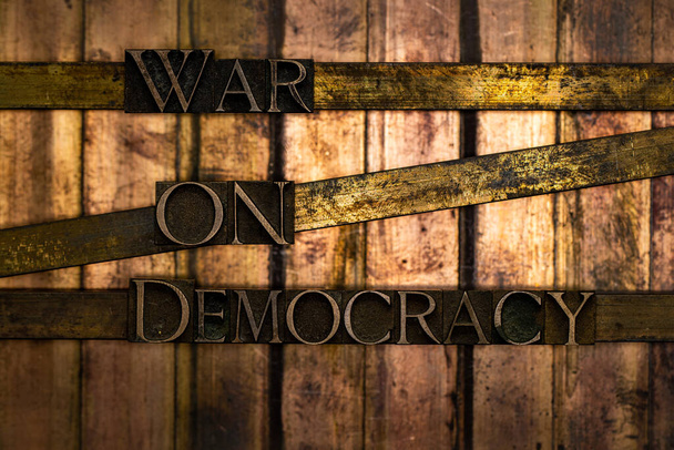 Photo of real authentic typeset letters forming War On Democracy text on vintage textured silver grunge copper and gold background - Photo, Image