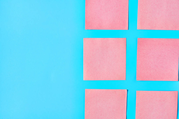 Rows of pink square blank paper stickers on blue background. Copy space. Top view - Zdjęcie, obraz