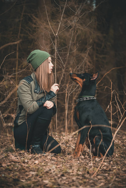 Young girl playing with doberman dog in the forest - Fotó, kép