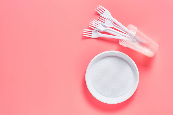 Disposable plastic utensils on pink background. Concept of save environment, ecology, recreation on picnic, party and other events. Copy space. Top view - 写真・画像