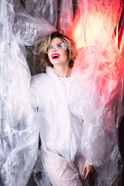 Beautiful model on the background of cellophane with red light, art photography, red lips, the beauty of lipstick. Beautiful scientist woman, world problem of cellophane pollution - 写真・画像