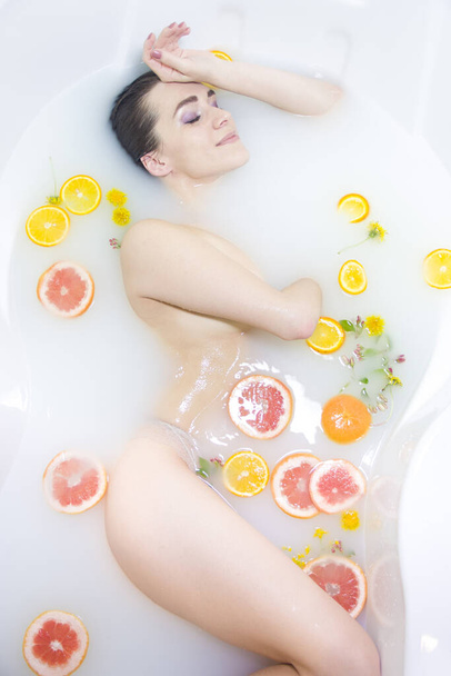 Girl in a milk bath, Spa treatments. An attractive girl takes a bath with milk and flowers. Spa treatments for skin rejuvenation - Photo, Image