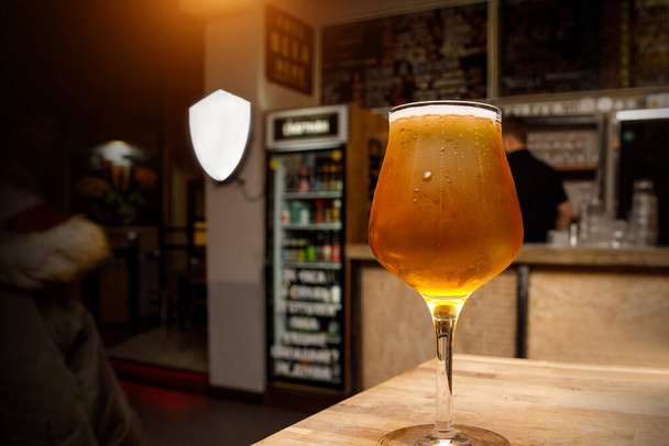 Cerveza ligera en un vaso de tulipán, interior del pub en el fondo
. - Foto, imagen