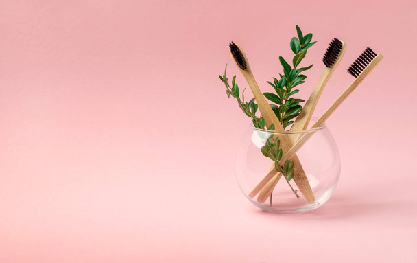 コピースペース付きピンクの背景にガラスカップに3本の竹、木製のブラシ。概念医学廃棄物ゼロリサイクル. - 写真・画像