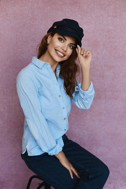 Happy charming model girl smiling wide. Emotional young woman with surprised facial expression. Portrait of delighting girl in a blue shirt, jeans and a cap on a pink background. - Fotografie, Obrázek