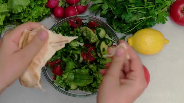 Top view of female hands putting pita bread into Fattoush slad - Footage, Video