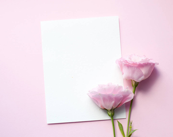 Een vel papier ligt horizontaal op roze papier, bloemen van eustoma (lisianthus) Bovenaanzicht, Kopieer ruimte. Onderwerp Moederdag, Gezinsdag, Valentijnsdag - Foto, afbeelding
