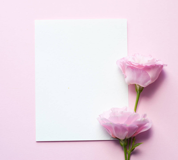Bir kağıt parçası yatay olarak pembe kağıdın üzerinde uzanır, östoma çiçekleri (lisianthus) Üst görünüm, uzayı kopyala. Anneler Günü, Aile Günü, Sevgililer Günü - Fotoğraf, Görsel