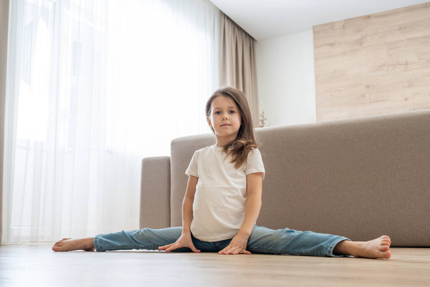Little girl doing split in living room at home - Фото, изображение