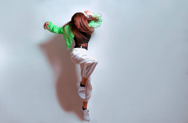 Dívka tančí v zeleném saku, tluče světlo, módní teenager se hýbe, směje se, tancuje, paří. Bruneta s dlouhými vlasy. Dívka v letu, skákání. - Fotografie, Obrázek