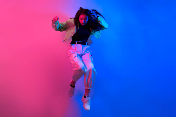 Brunetka tańczy w neonie, tancerka w czerwono-niebieskim. Hip-hopowa dziewczyna, impreza, uśmiech. Model w locie, skoki. - Zdjęcie, obraz