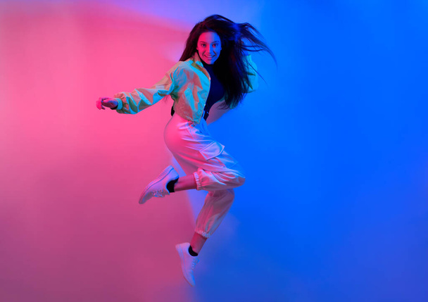 De brunette danst in neon, de danseres in rood-blauw. Hip hop meisje, feest, glimlach. Model tijdens de vlucht, springen. - Foto, afbeelding