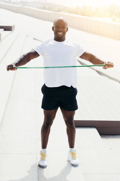 The black athlete is training with elastic sports tape on the street. Stretch a tape expander on the chest level. - Foto, afbeelding