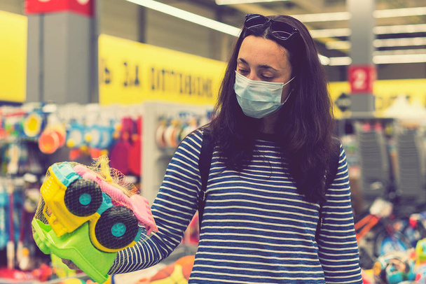 La mujer con la máscara protectora en el supermercado escoge los juguetes infantiles. tonificado. - Foto, imagen
