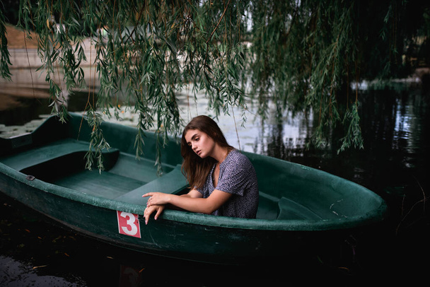 Een jong meisje zit in een oude boot tegen een achtergrond van waterlelies op een zomerdag - Foto, afbeelding