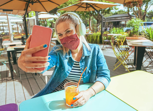 Menina no bar tomar uma selfie com um smartphone com sua máscara facial em como uma proteção para o tempo coronavírus - Adolescente refrigeração fora e desfrutar de uma bebida fria - Estilo de vida de covid-19
 - Foto, Imagem