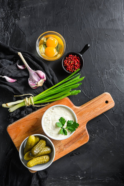 Tartar Sauce with organic ingredients pickles, capers, dill, parsley, garlic, lemon and mustard rose peppercorns on a dark black stone concrete background. Horizontal, top view vertical. - Foto, Bild