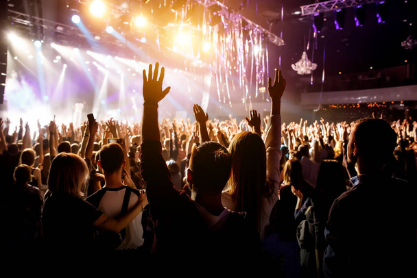 Muž s rukama nad hlavou na koncertě své oblíbené skupiny. Světlo z jeviště - Fotografie, Obrázek