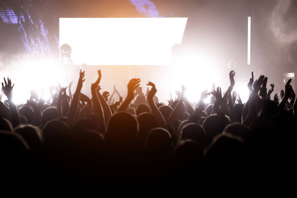 Salle de concert avec une scène éclairée et des silhouettes de personnes lors d'un concert
. - Photo, image