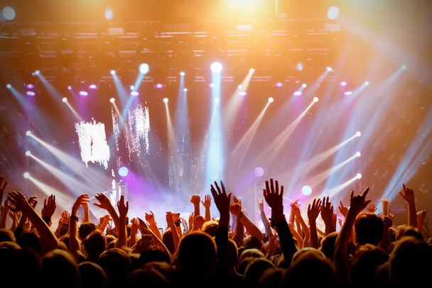 Concertzaal met een verlicht podium en mensen silhouetten tijdens een concert. - Foto, afbeelding