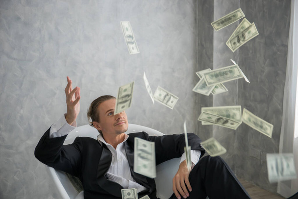 Πλούσιος επιχειρηματίας ξαπλωμένος σε μπανιέρα γεμάτος χαρτονομίσματα. Επιχειρηματική ιδέα επιτυχίας. - Φωτογραφία, εικόνα