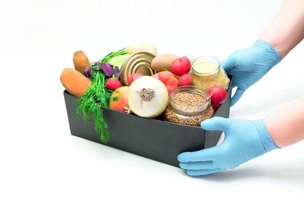 donation help box full of supplies, vegetables,cereal and fruits. Volunteer in protective medical hand gloves holding food box for delivery charity isolated with copy space. - Foto, afbeelding